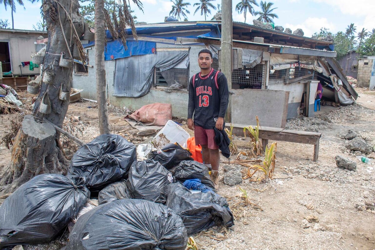 A young man looks at the camera. Next to him are a pile of rubbish bags.