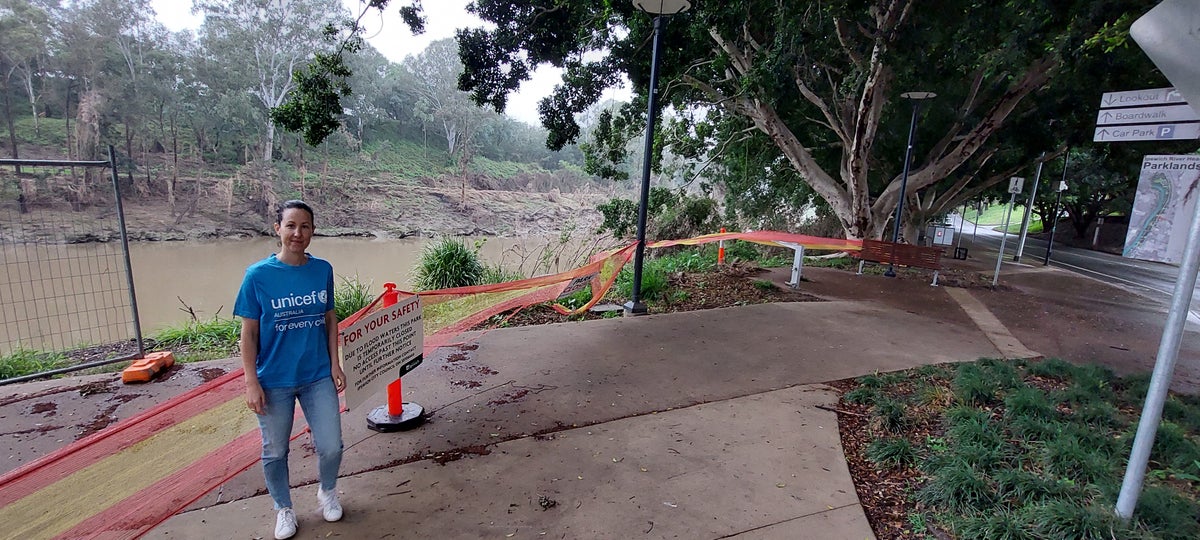 Adrienne stands by the river showing flood damage