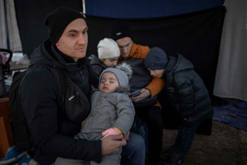 In Ukraine, 2022, Mikhail holds his daughter, while sitting next to his other children inside a tent in a reception area on the border of Moldova after escaping violence in their village. © UNICEF/UN0607407/Modola
