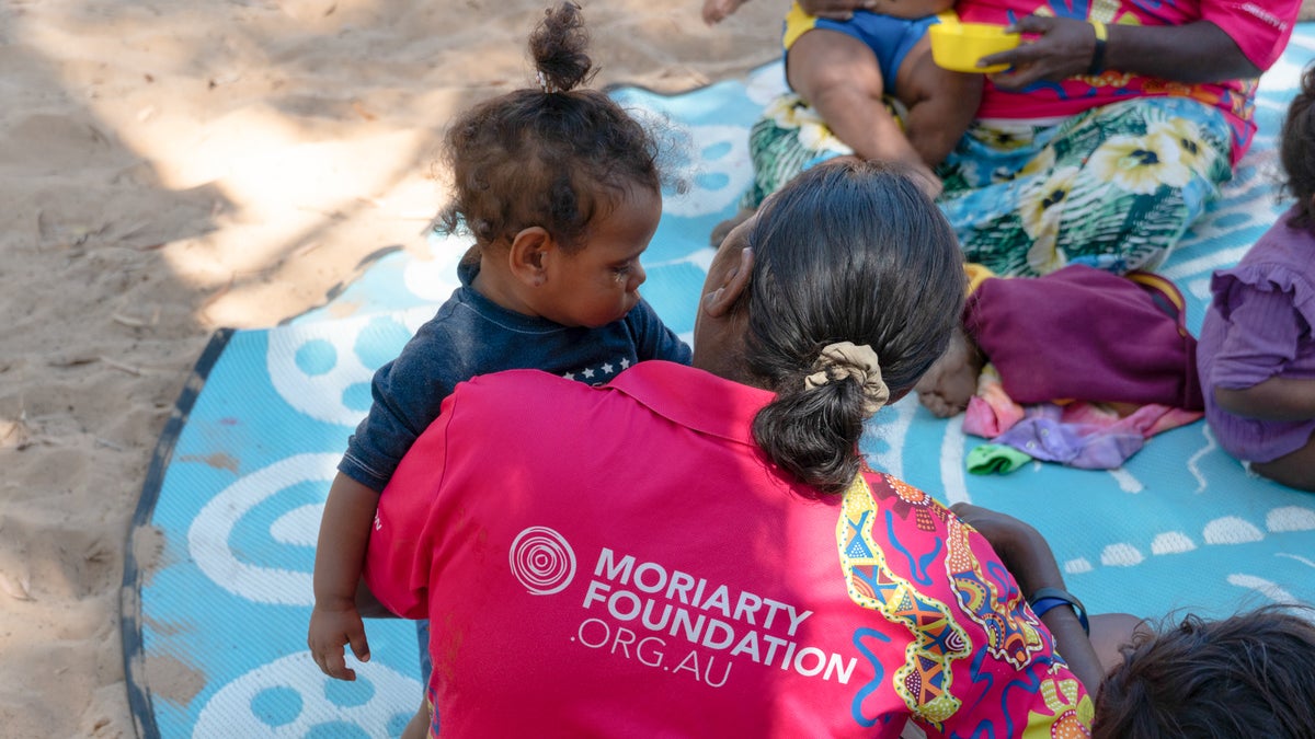 A woman sitting on the ground holding a toddler in her arms.