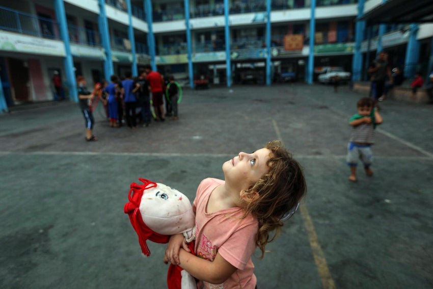 At a school in the Gaza Strip, a five-year-old girl clutches her doll as she gazes up at the sky. 
