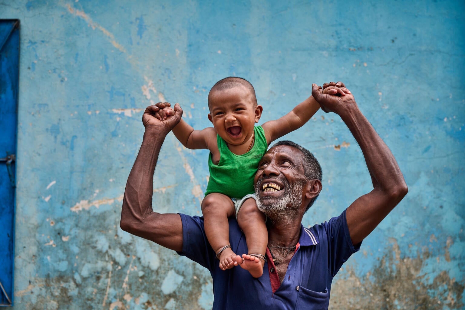 In Bangladesh, a grandfather holds his grandchild up on his shoulder