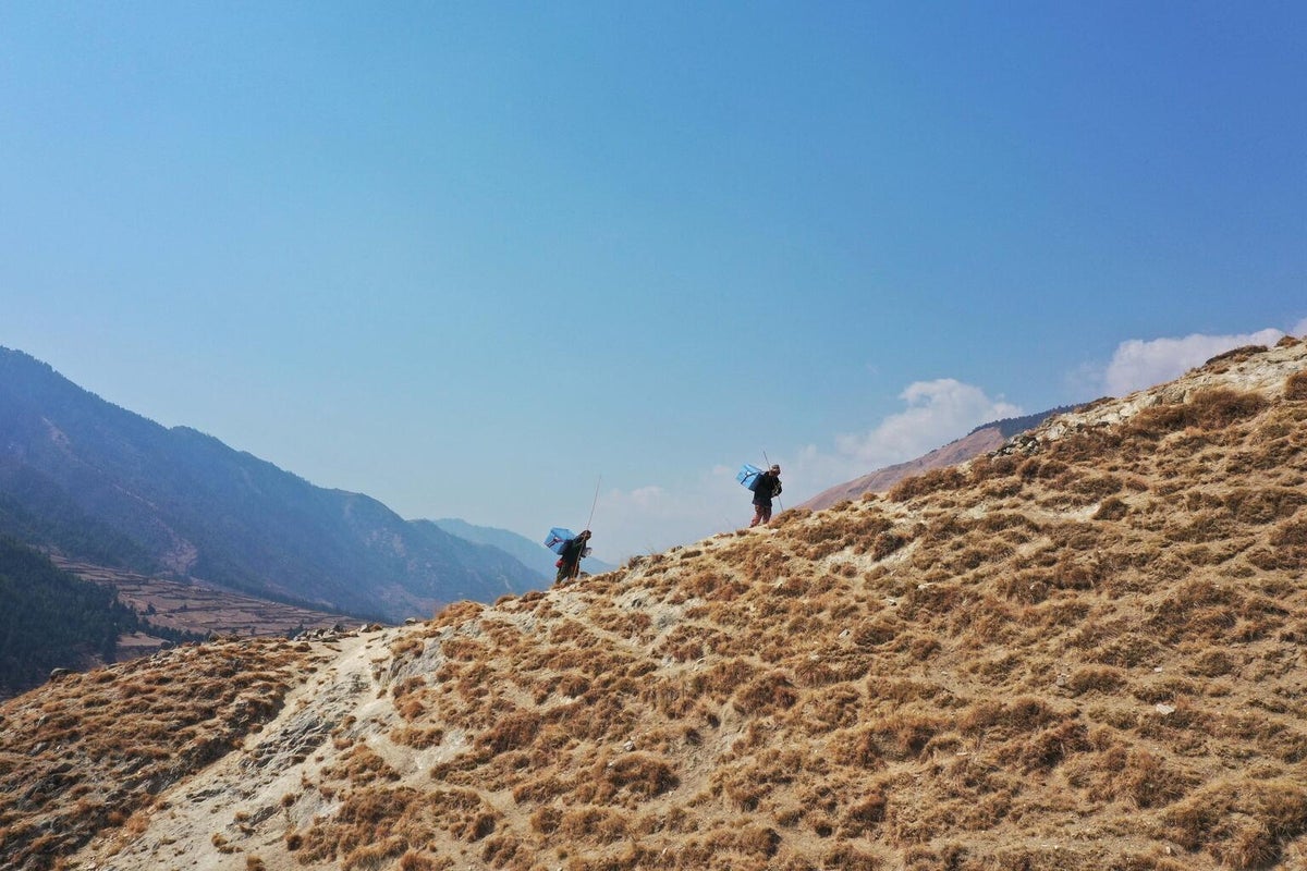 Two men are walking through a deserted mountain trail. They are carrying an cooler box on their bags with the UNICEF logo