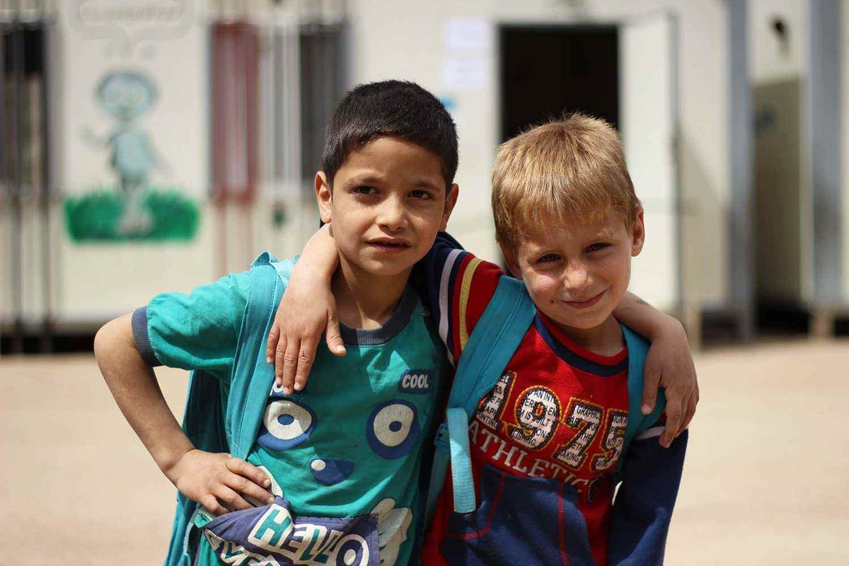 boys with arm around each other, wearing backpacks, smiling