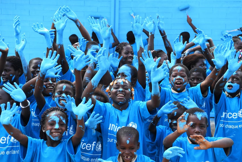 A group of children with UNICEF t-shirts raise their blue-painted hands