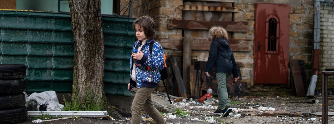 Two young children walking through a street of rubble. 