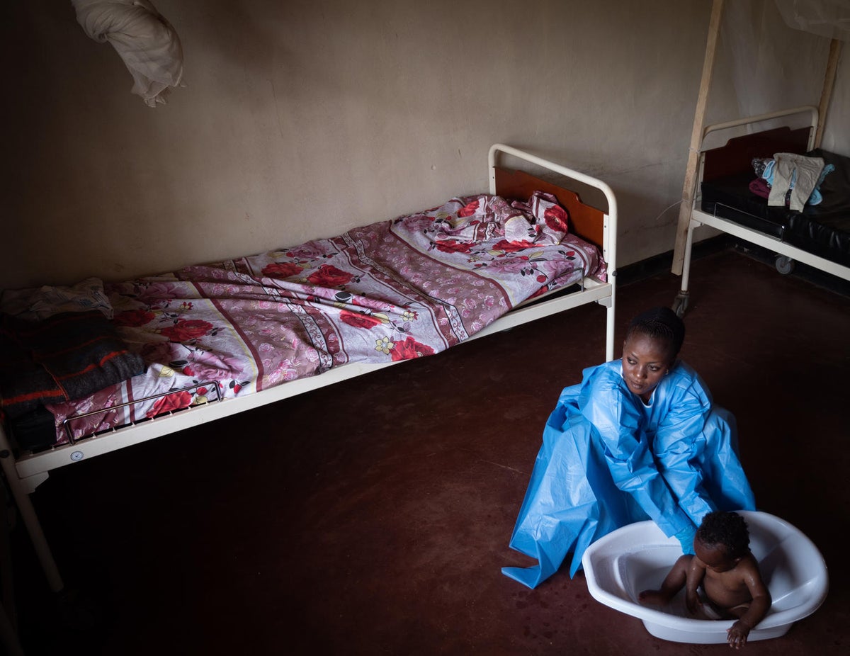 A woman is wearing a protective gown and gloves while bathing a baby on a basin.