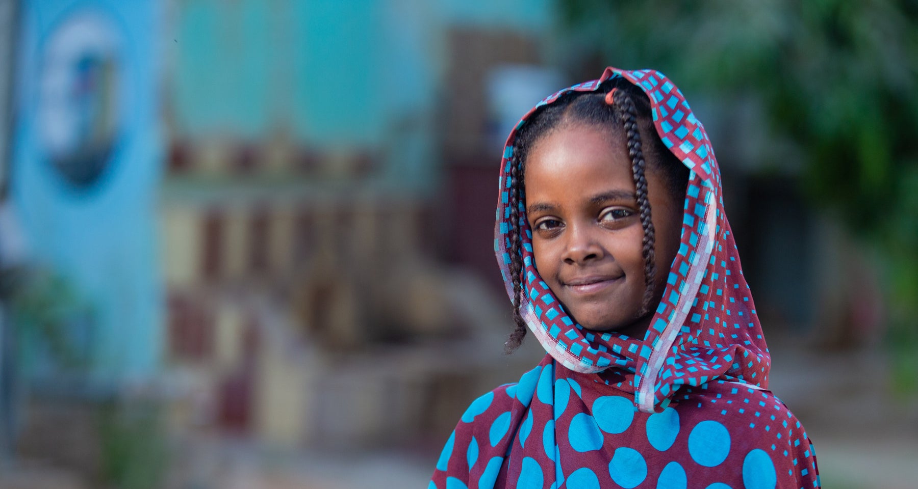 A girl stands with resilience outside a UNICEF-supported safe learning space for displaced children in Sudan.