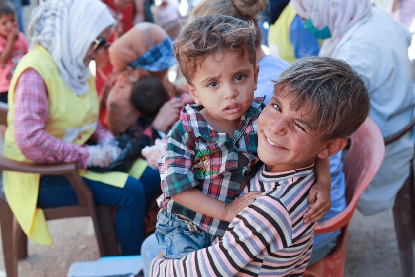 A young boy holds a toddler in his arms and winks to the camera.