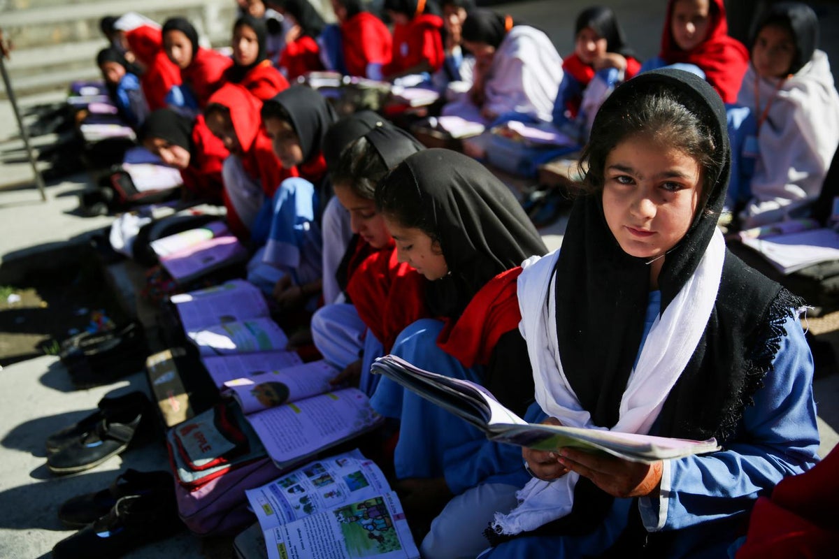 A group of girls are reading a book each. One of them is looking at the camera.