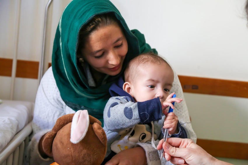 A little Afghanistan boy resting on his mother's lap and looking at the camera.