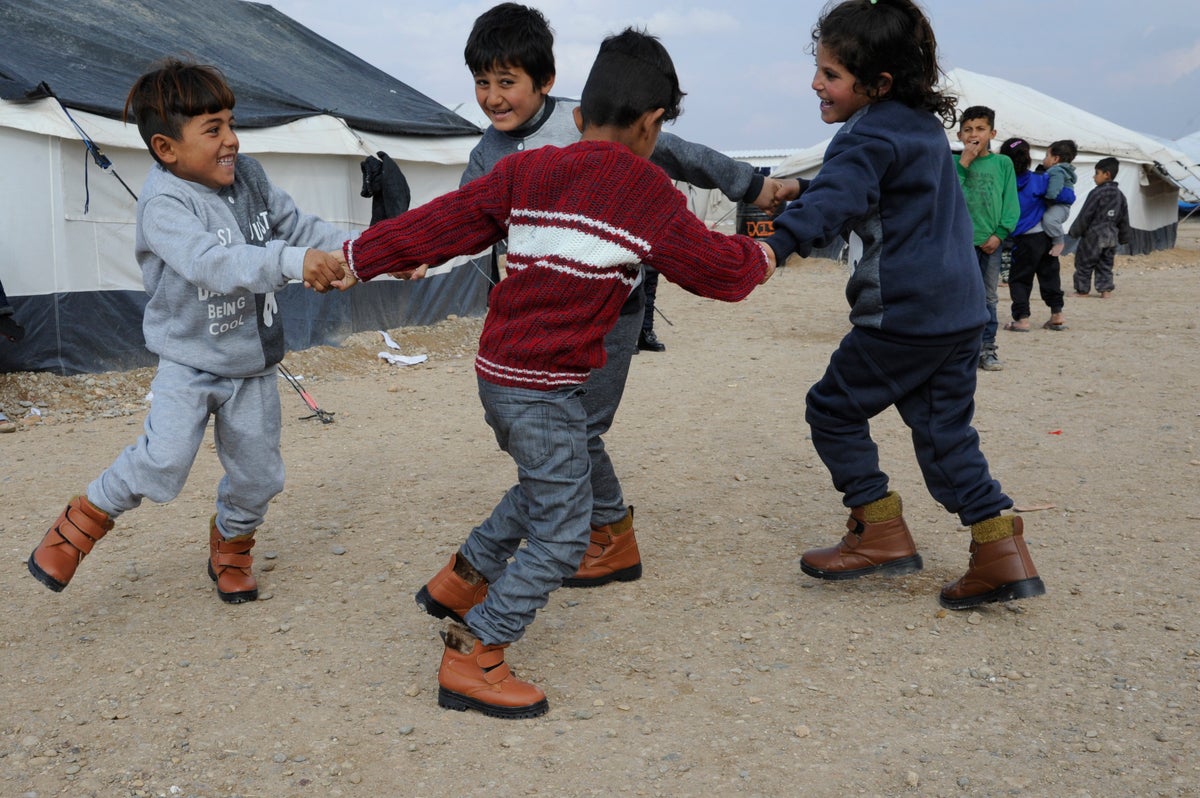 Children wearing items from a winter kit distributed by UNICEF, play in a camp in the Syrian Arab Republic