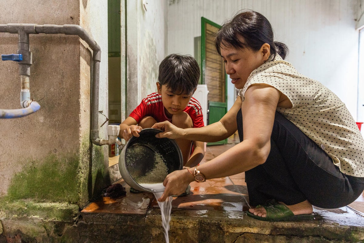 A woman and her son prepare rice together at home, working side by side.