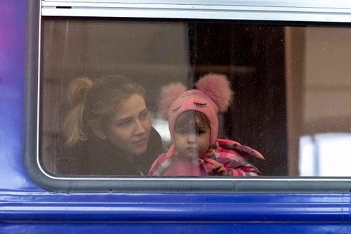 In Ukraine, 2022, a little girl peers out from a window as she waits inside an evacuation train to Poland, at Lviv train station. 