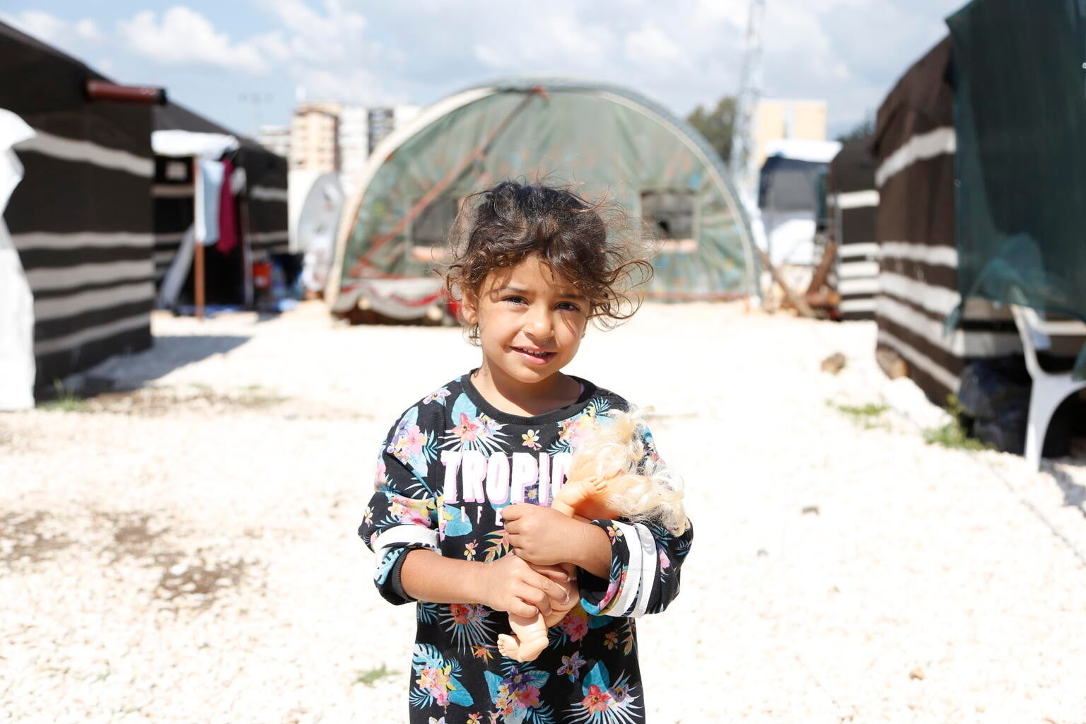 A young girl from Turkiye holding her doll and smiling at the camera.