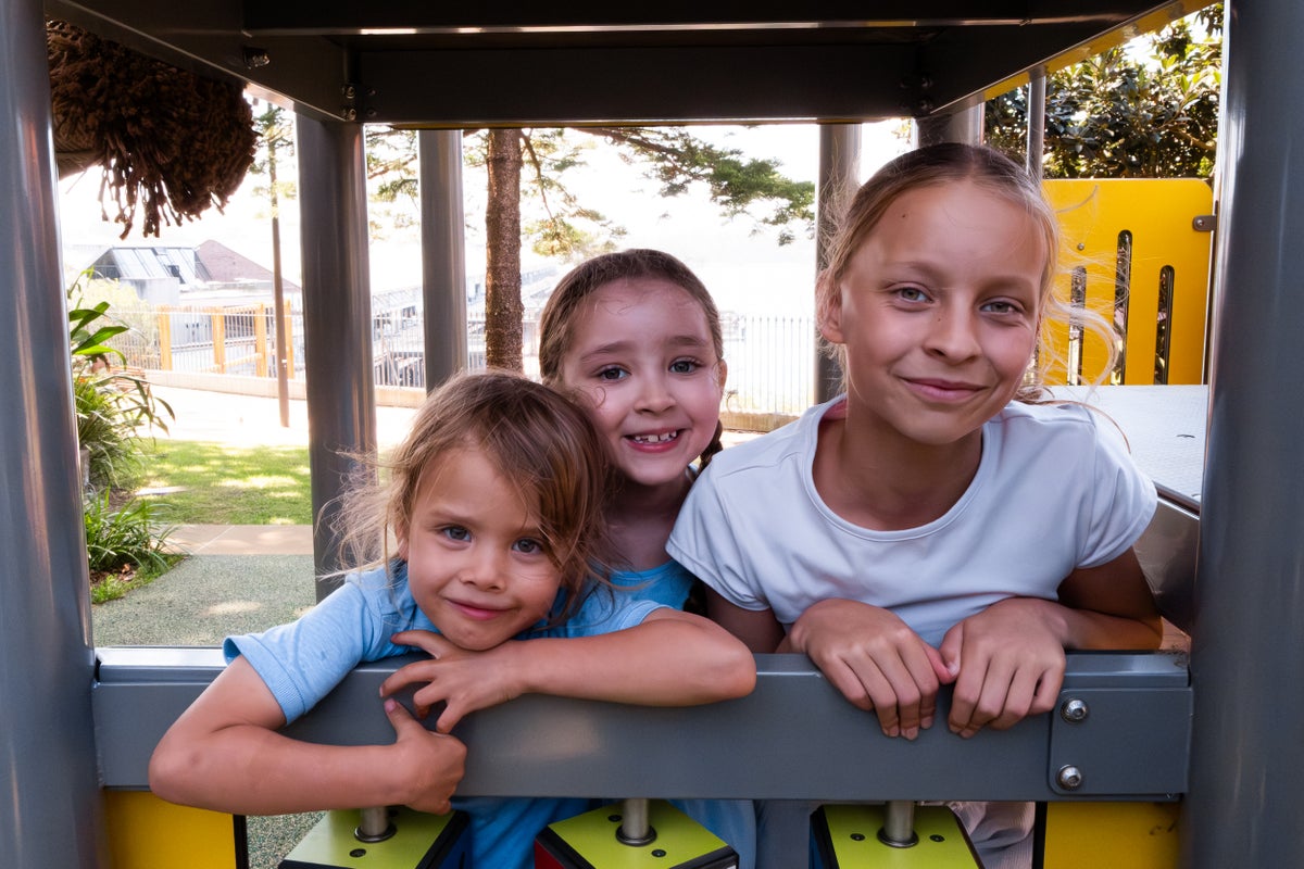 Three children of various ages pose for a photo in a playground.