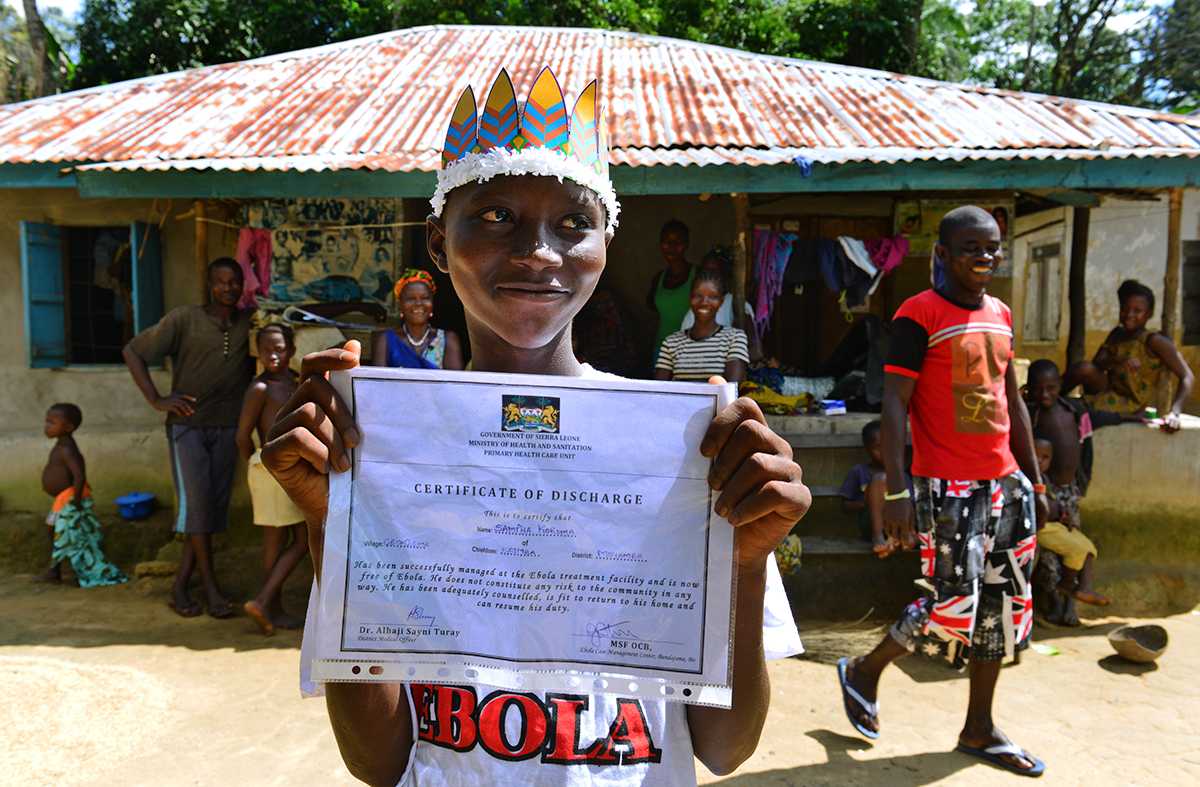 Sanfa holds up his survivor certificate in front of his home. 