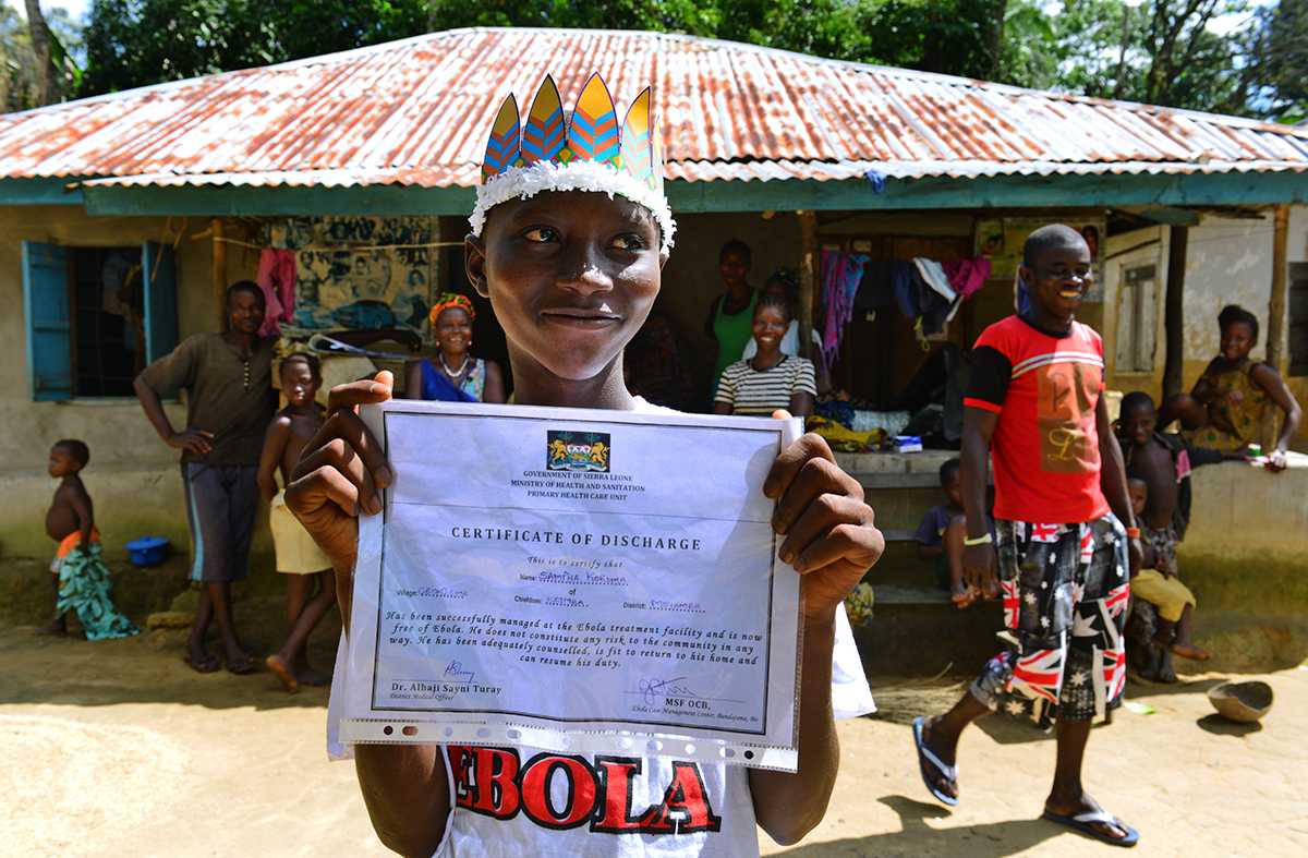 Sanfa holds up his survivor certificate in front of his home.