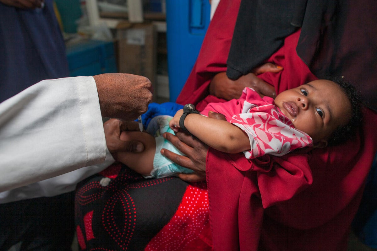 A baby girl on her mum's arms is about to be vaccinated by a health worker.