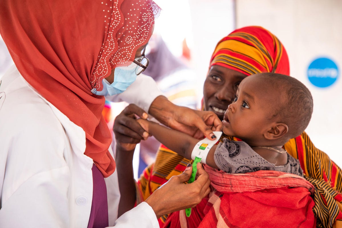 A woman is holding a baby while a health worker assesses them for malnutrition.