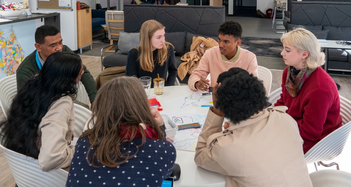 A group of young people sit around a table and participate in a group discussion.