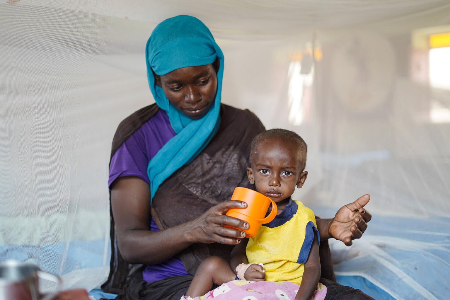 A Sudanese mother feeding her child therapeutic milk to treat malnutrition. 