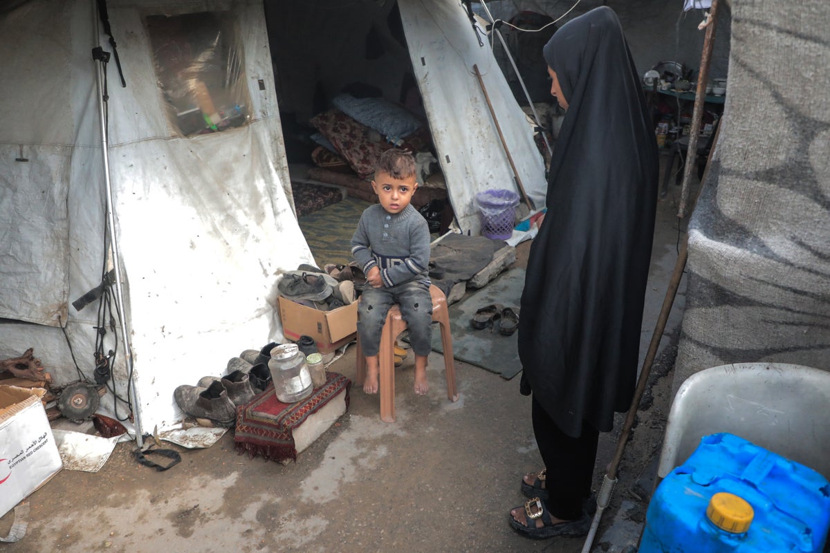 A three-year-old boy and his mother sit outside their tent.