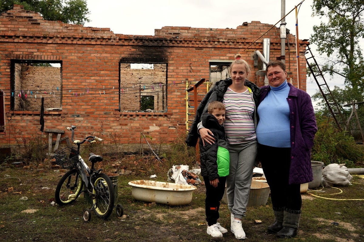 A young boy stands with his mother and grandmother out the front of their family home, which has been destroyed during the ongoing conflict with Russia. 