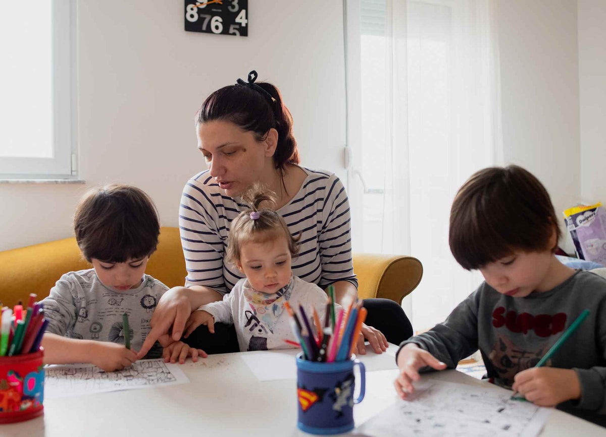 Aleksandra helps her twins Maksimm, 5, and Jan, 5, with learning activities as she holds their sister Stela, 15 months.