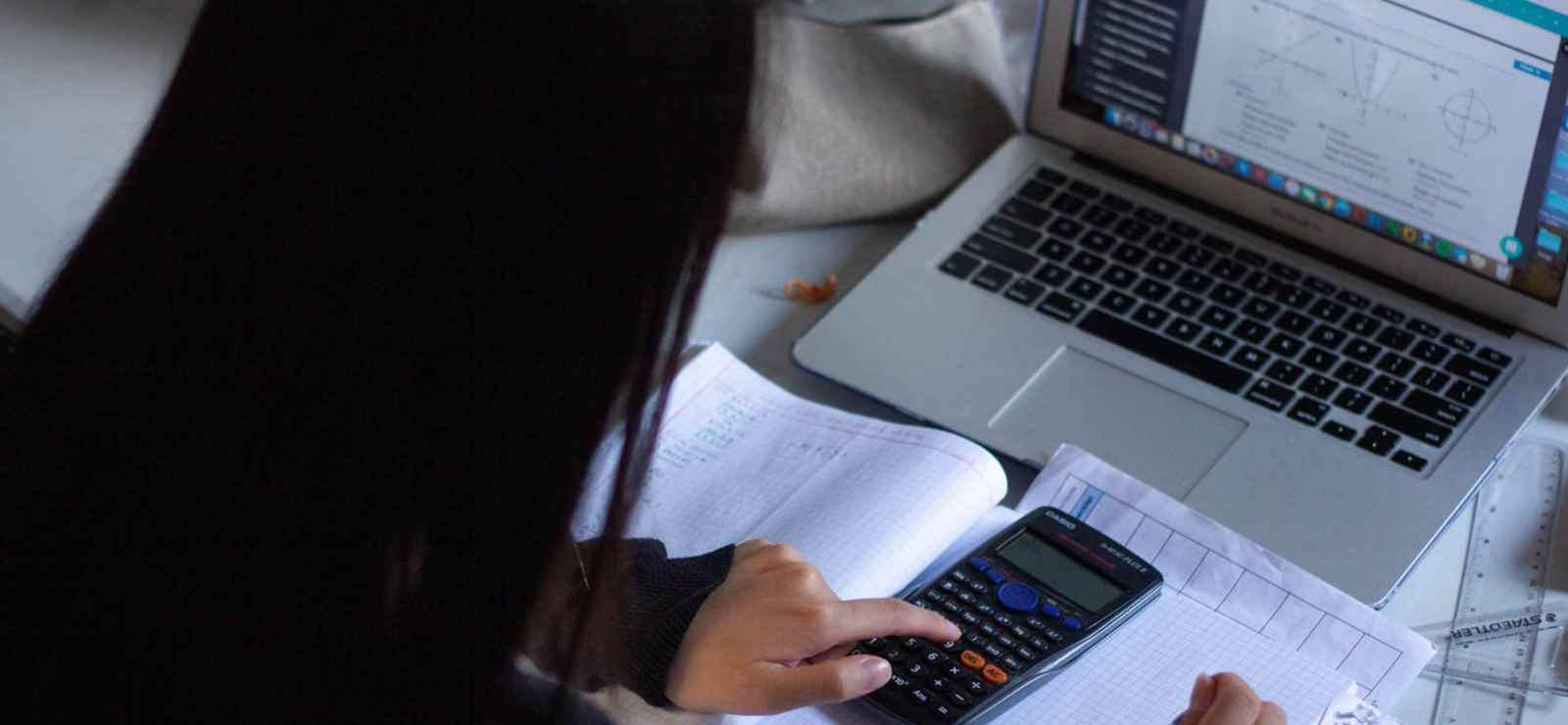 Student at desk in front of computer using calculator