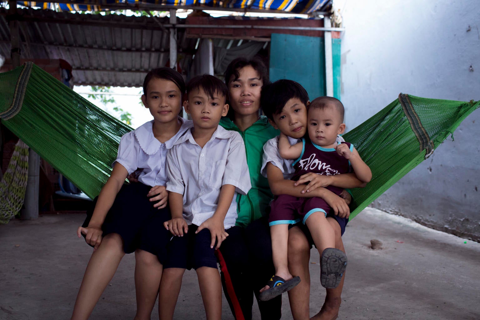 Tran Thi Ngoc Mai, 37, scrap collector, sits for a portrait with her three children and a neighbor's kid in front of their makeshift tin home in Ho Chi Minh city
