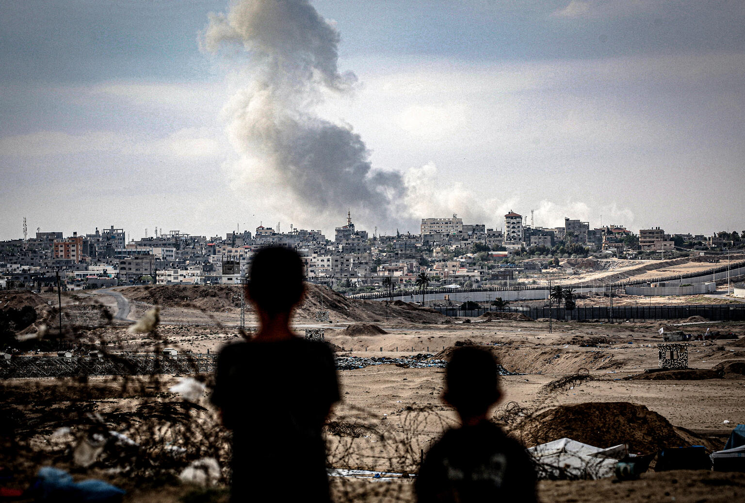 Two children standing and looking at smoke rising over Gaza.
