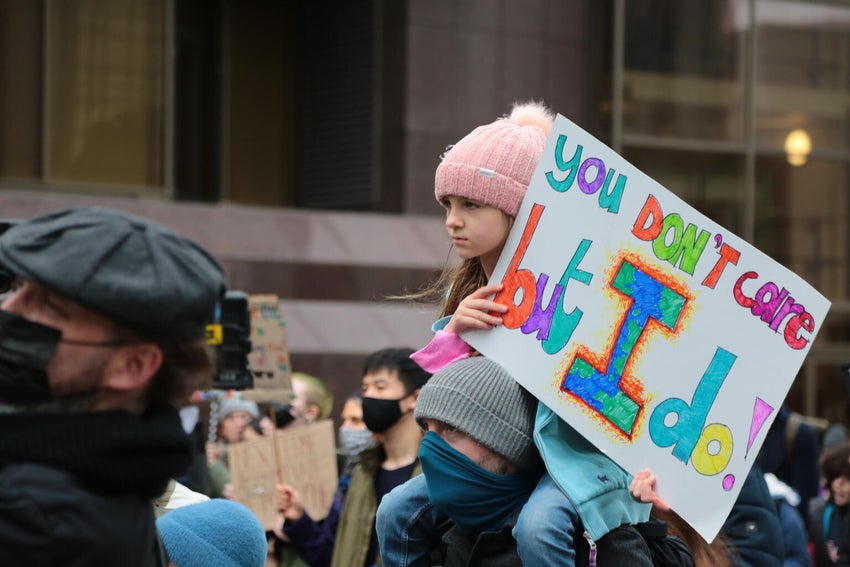 A young girl wearing a pink beanie holds a sign saying 'You don't care but I do' at a climate protest in Glasgow, Scotland.