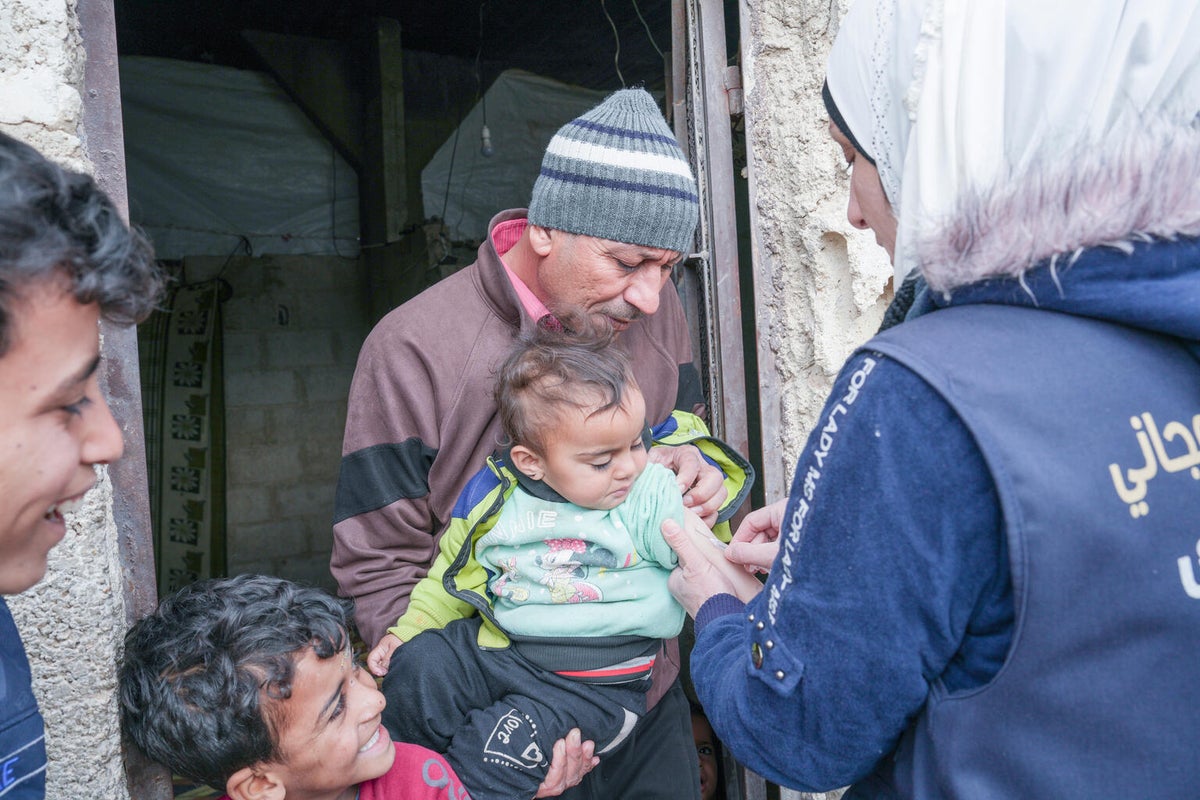 One-year-old Sidra receives her vaccine from a mobile health worker during an immunisation campaign in Syria.