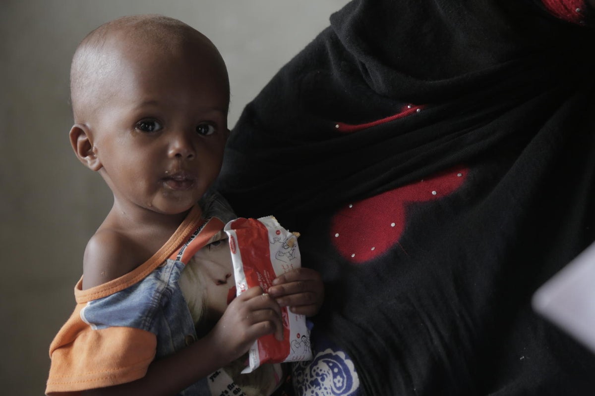 A young boy is on his mum's lap. He is holding a pouch of ready to use therapeutic food.