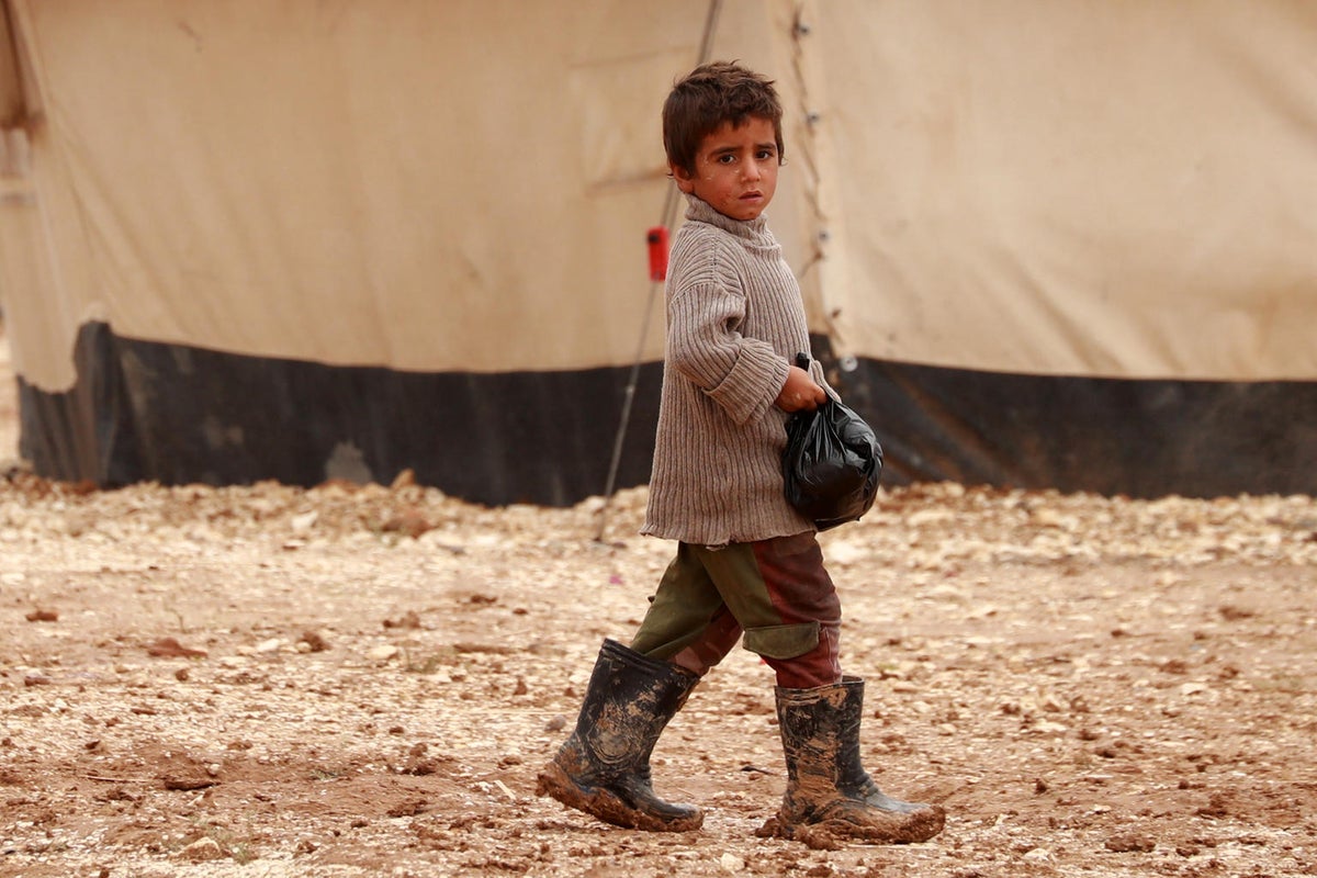 A young boy wearing muddy gum boots walks on a dirt road