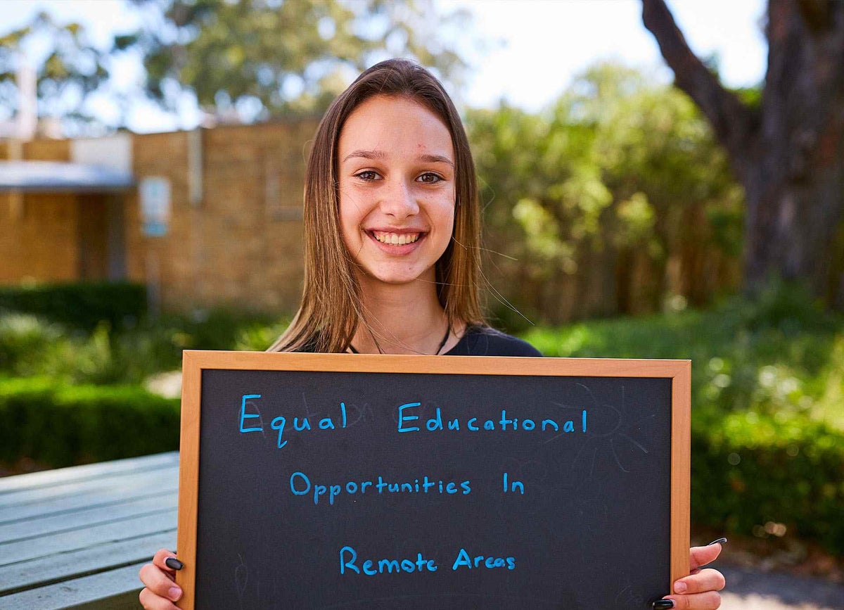 A teenage girl holds a chalkboard which says "Equal educational opportunities in remote areas