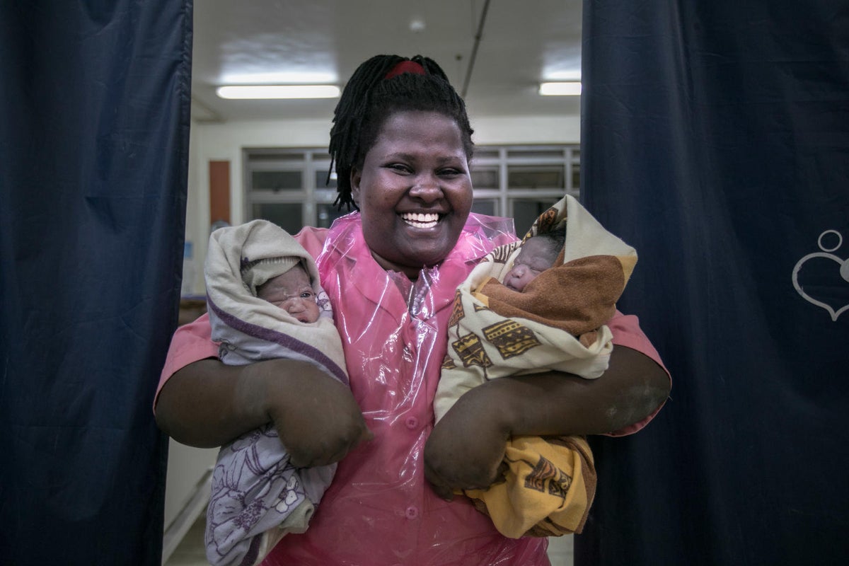 A woman is holding two babies in her arms. She has a big smile.