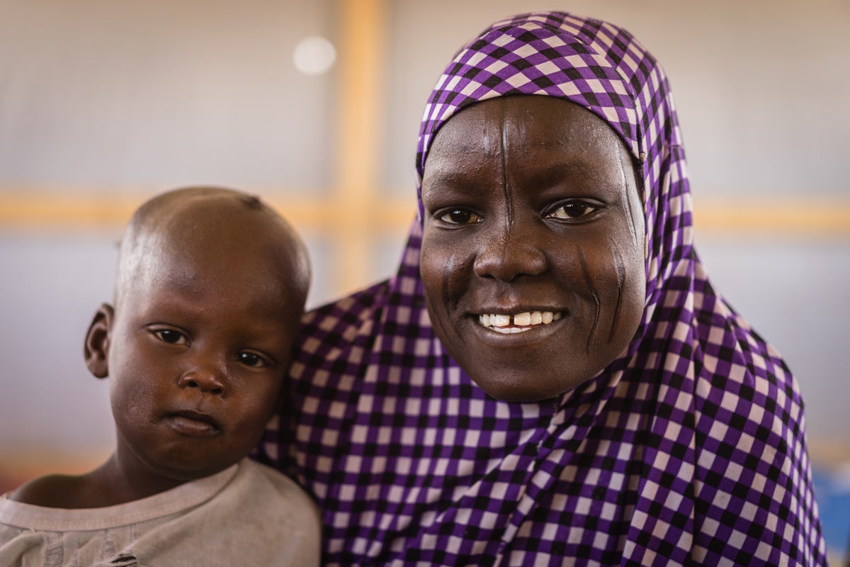 A young woman smiles to the camera. She is holding a baby.