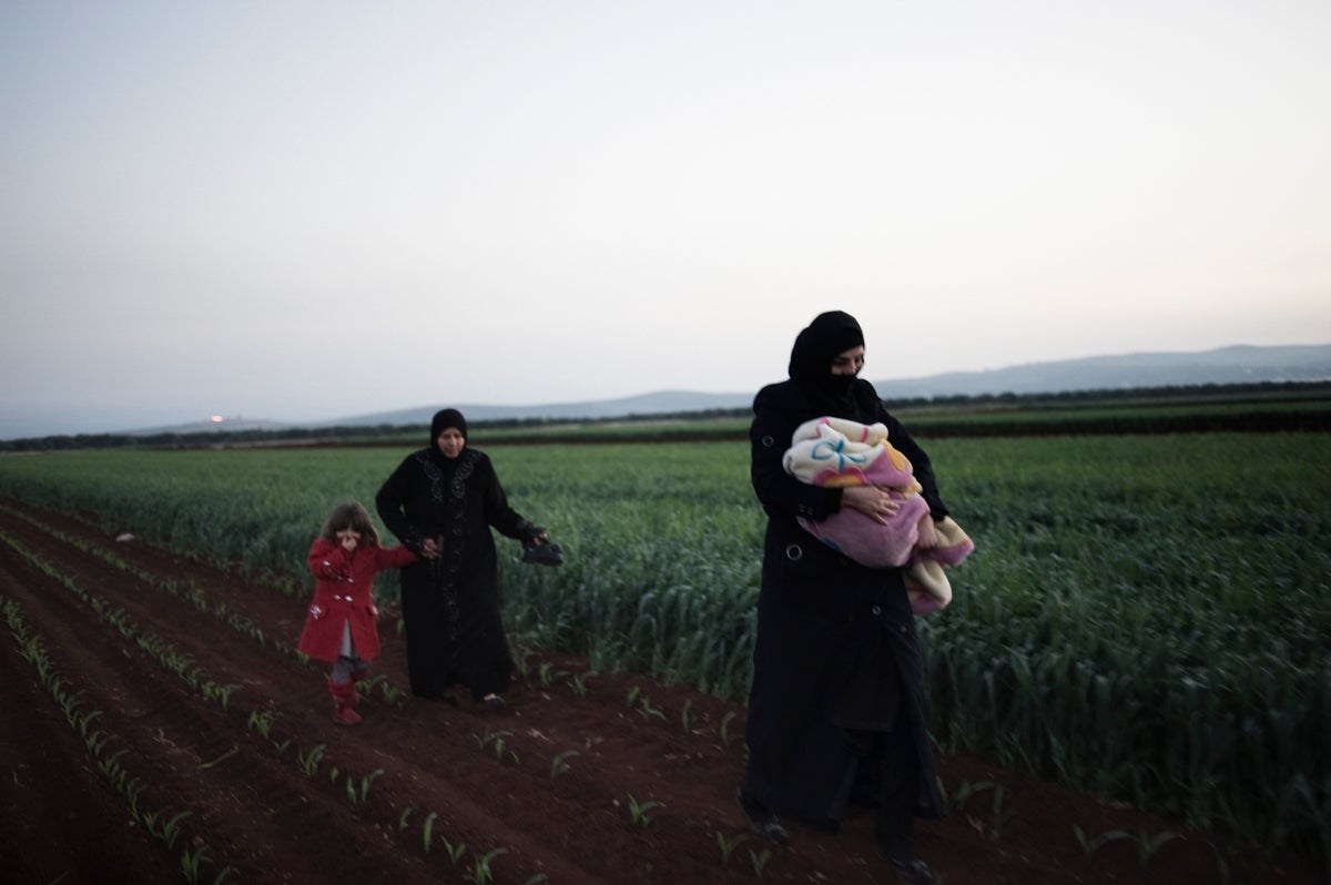 Children and women walk through a ploughed field in Syria