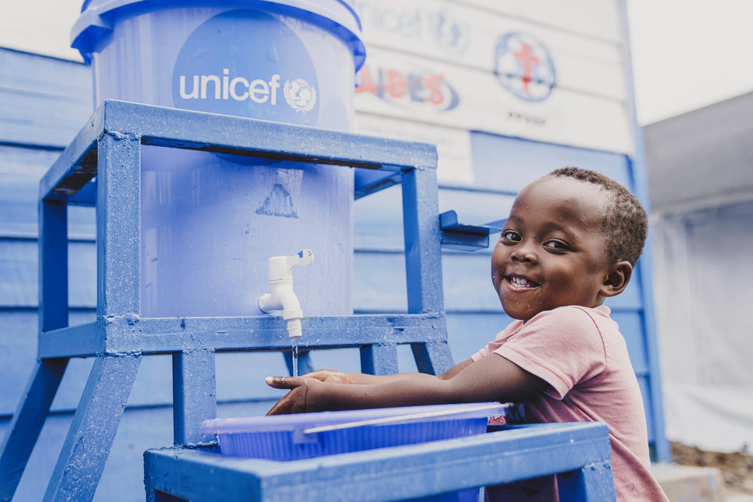 A young boy washing his hands at a water tank.