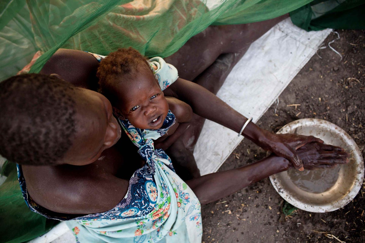 A woman washes her hands in dirty water while camping outside to register for a food ration card in Thanyang, South Sudan on March 21st, 2016. 