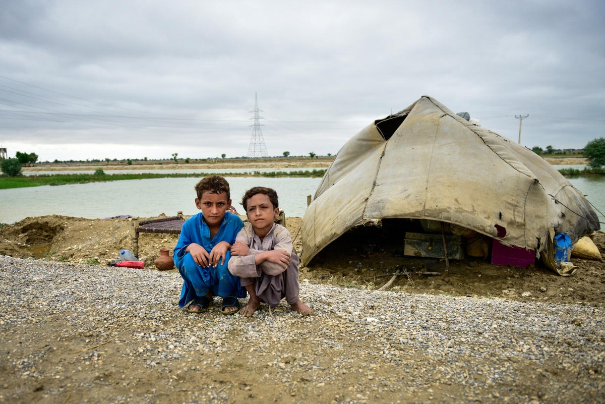 Two boys seating on the floor. Behind them, there's a makeshift tent.