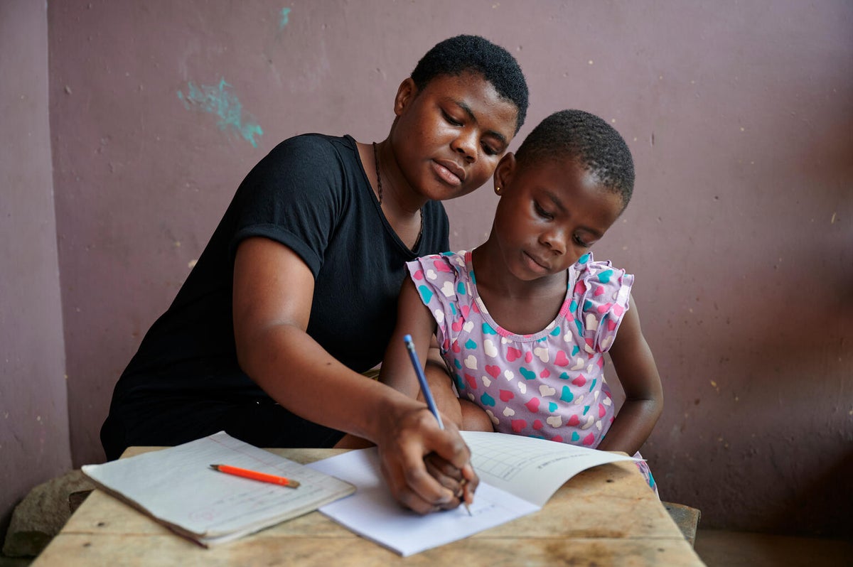 A young woman helps her young cousin with homework outside their home in Ghana.