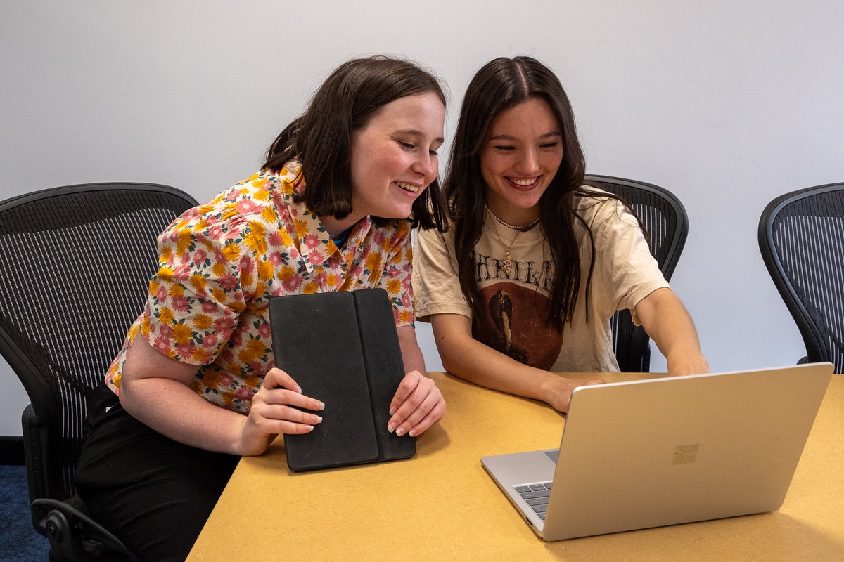 Two young girls look at a laptop together.