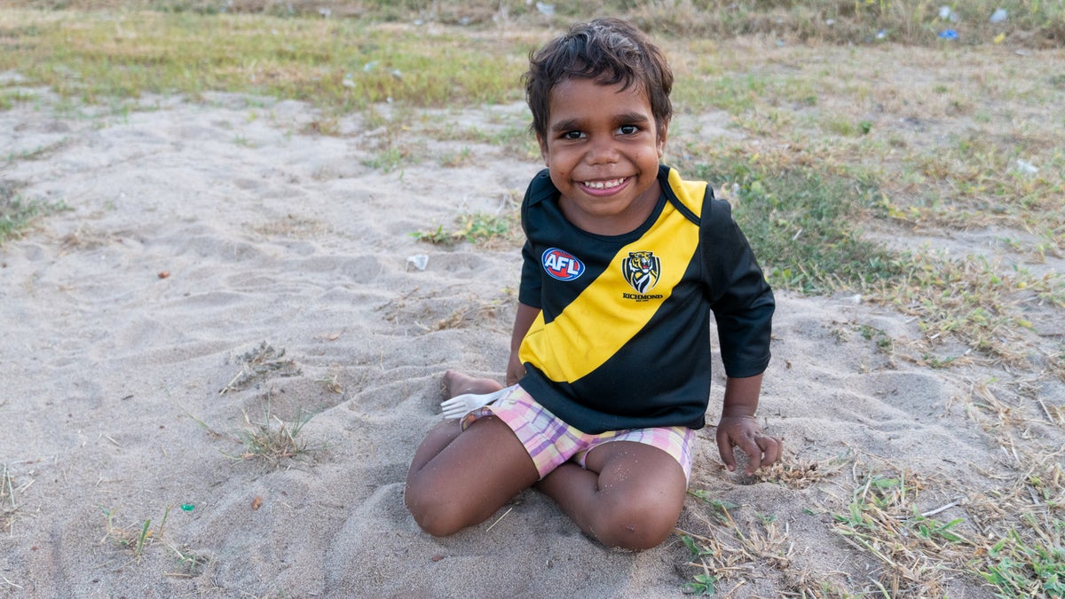 A young smiling boy sits on the grass.