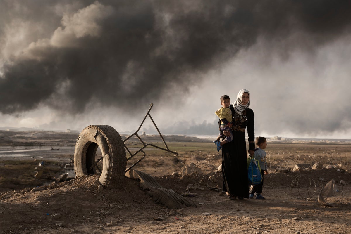 A woman with two young children is in a desolated land. 