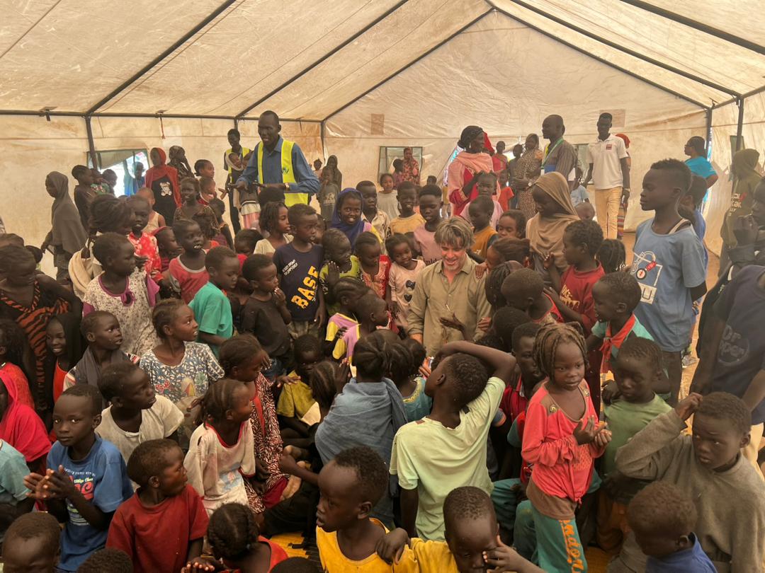 A smiling man with a group of children inside a large tent.