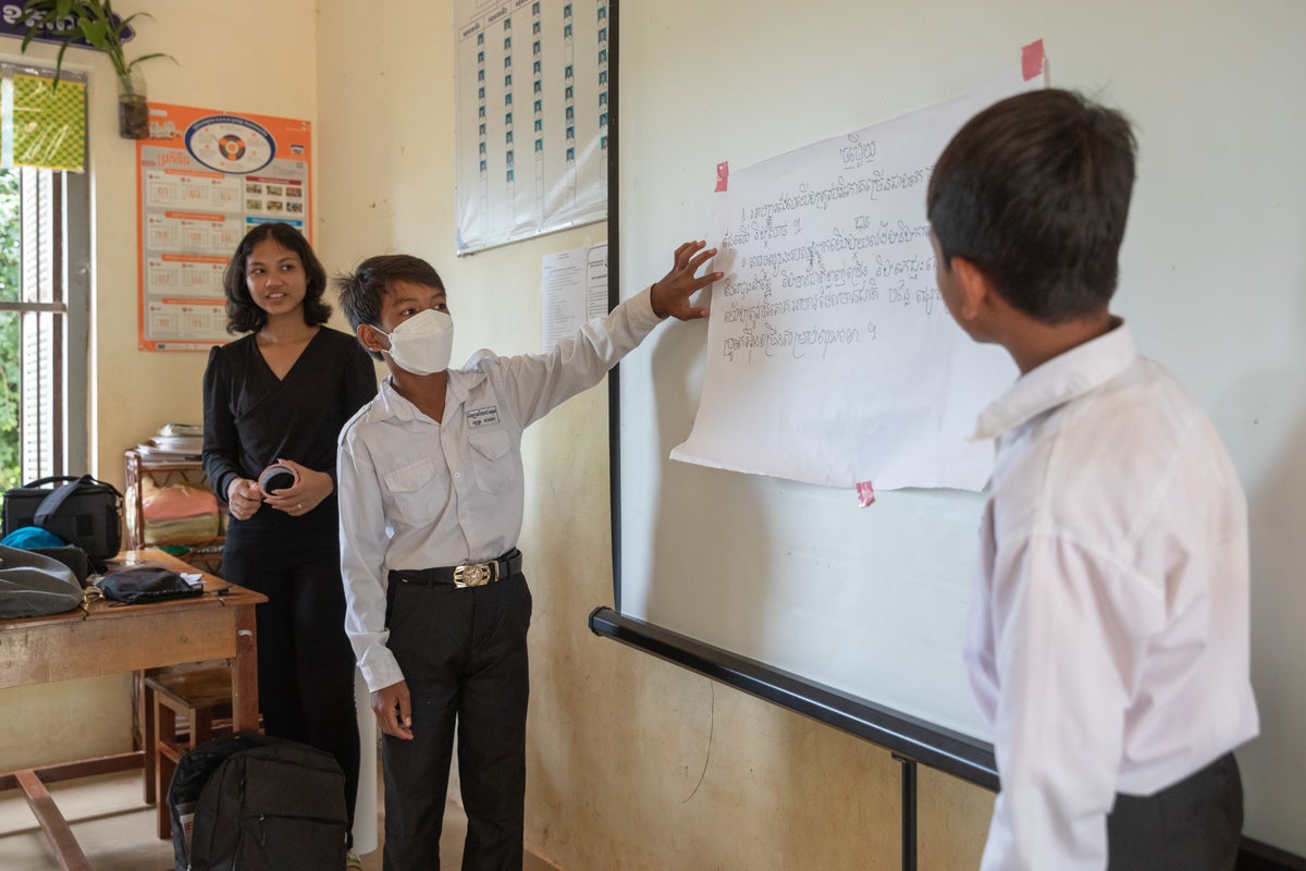 Students stands in front of a white board while other young people look on