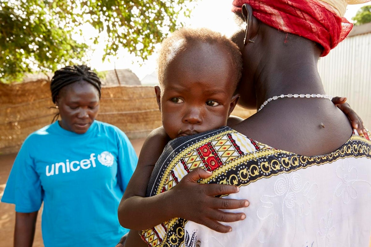 The toddler is in her mum's arms and she looks sad.